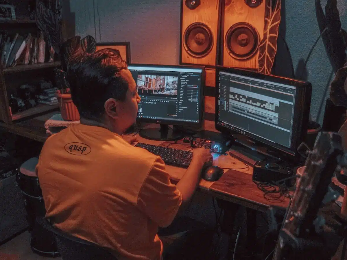 A male video editor sits at a desk and uses two video screens to adjust an AI generated video