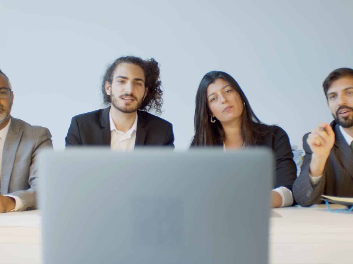 a group of business people sit in a line watching the laptop in the foreground that shows a B2B business video