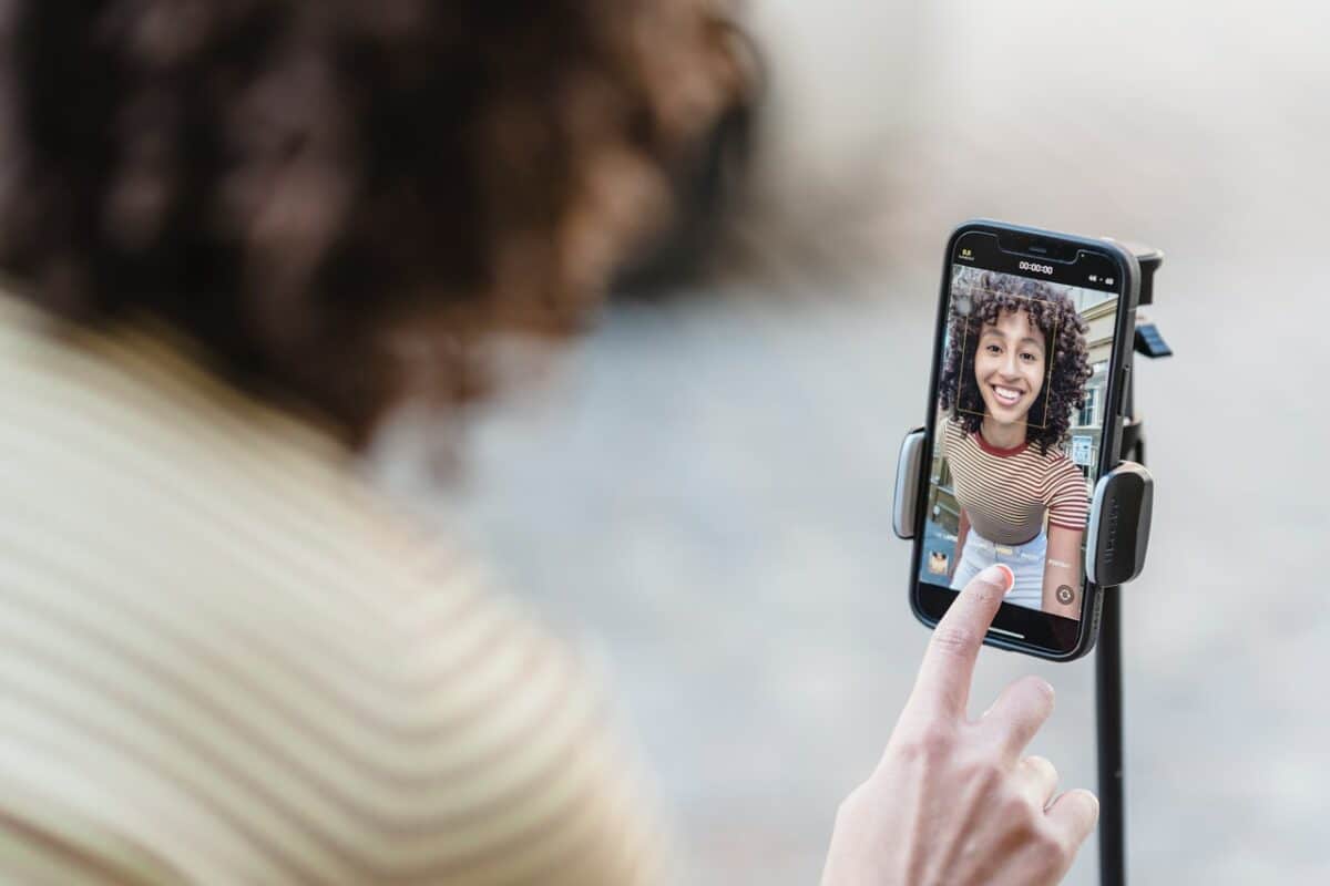 The view is of a smartphone on a tripodseen over a woman's shoulder as she bends down push the record button on the screen.