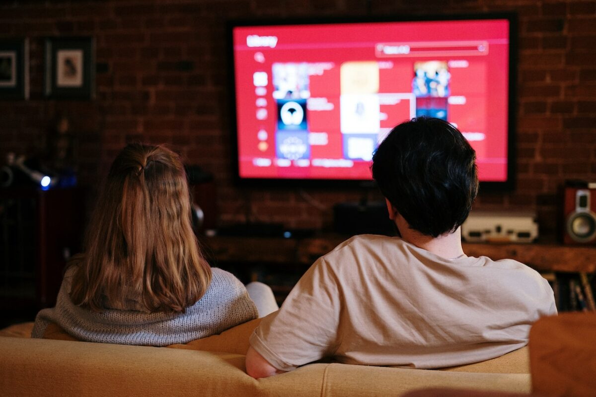 a man and a woman sit on a couch watching a television