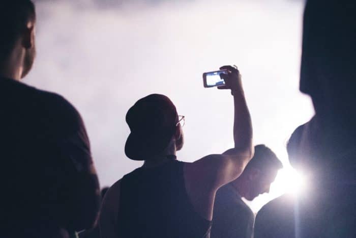 backlit man holding smartphone over his head