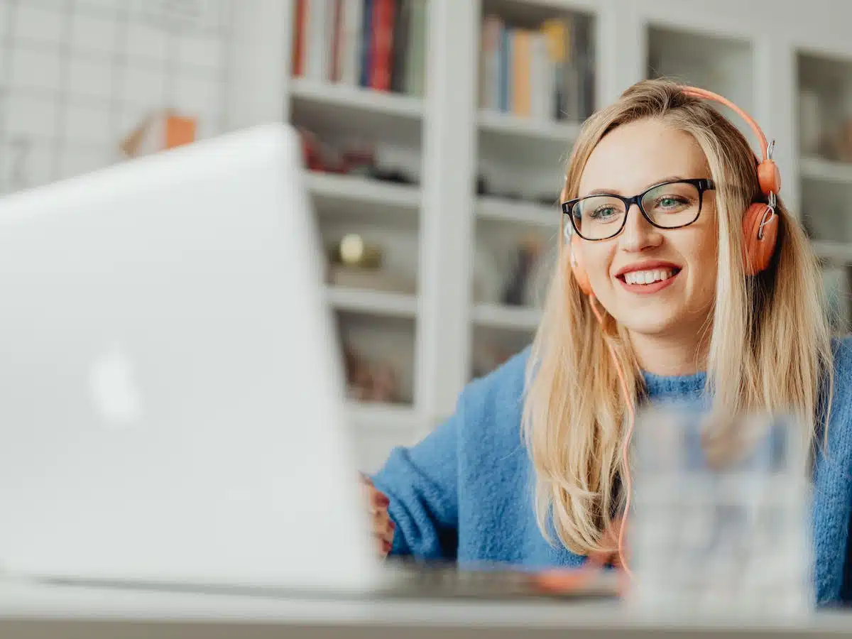 a woman wearing orange headphones watches a video on her mac