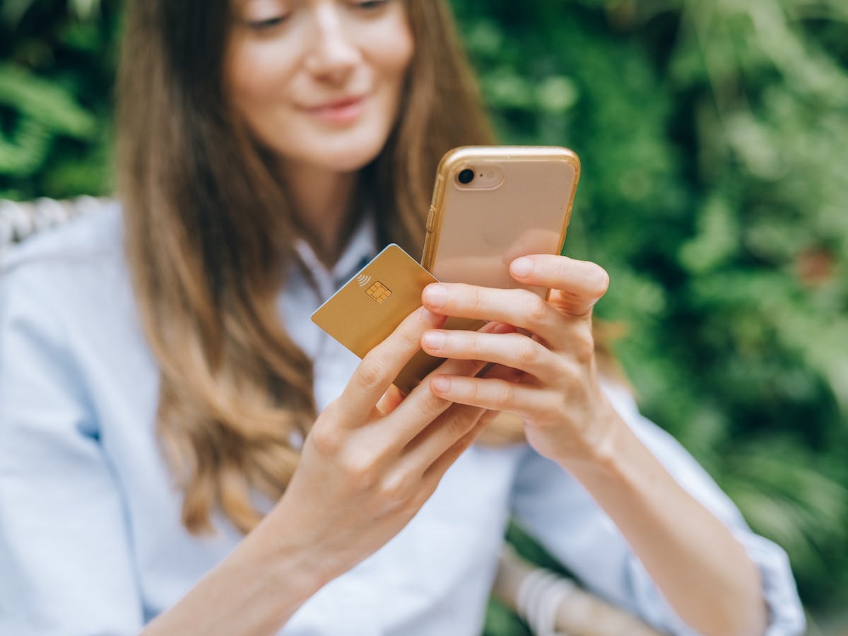 A woman looks at a video landing page on her smart phone, while holding a credit card