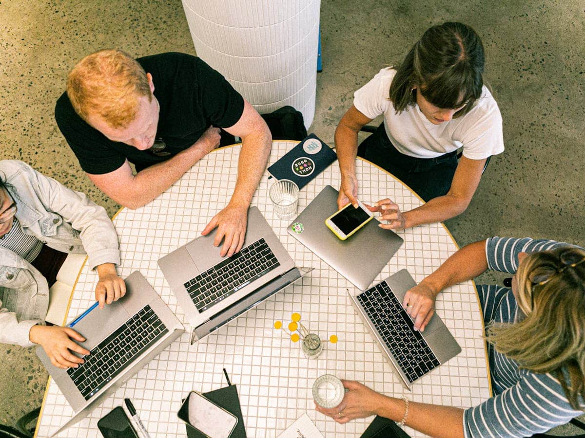 four people sit around a table using laptops to collaborate on a video production