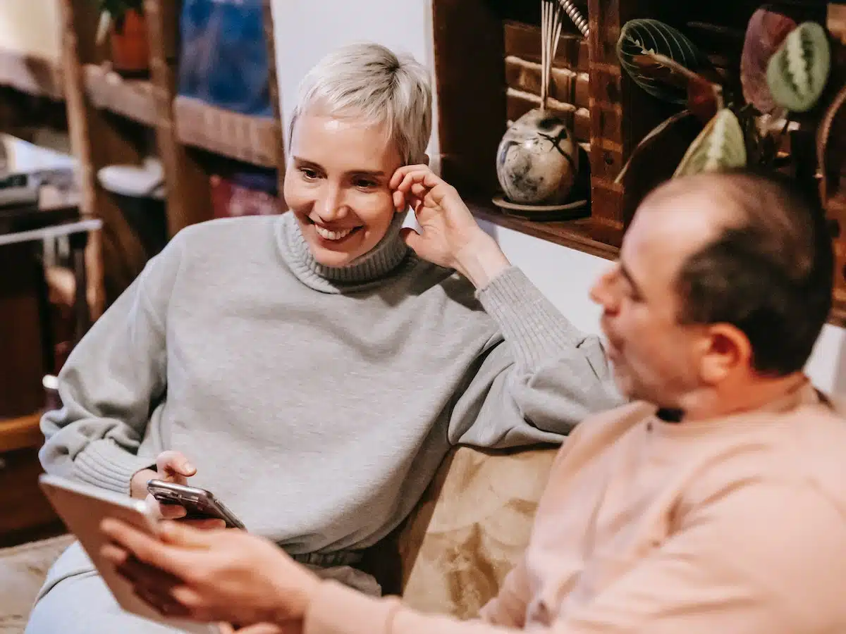 two people sitting on a couch. The woman is holding a cell phone and the man is showing her an email on his tablet.